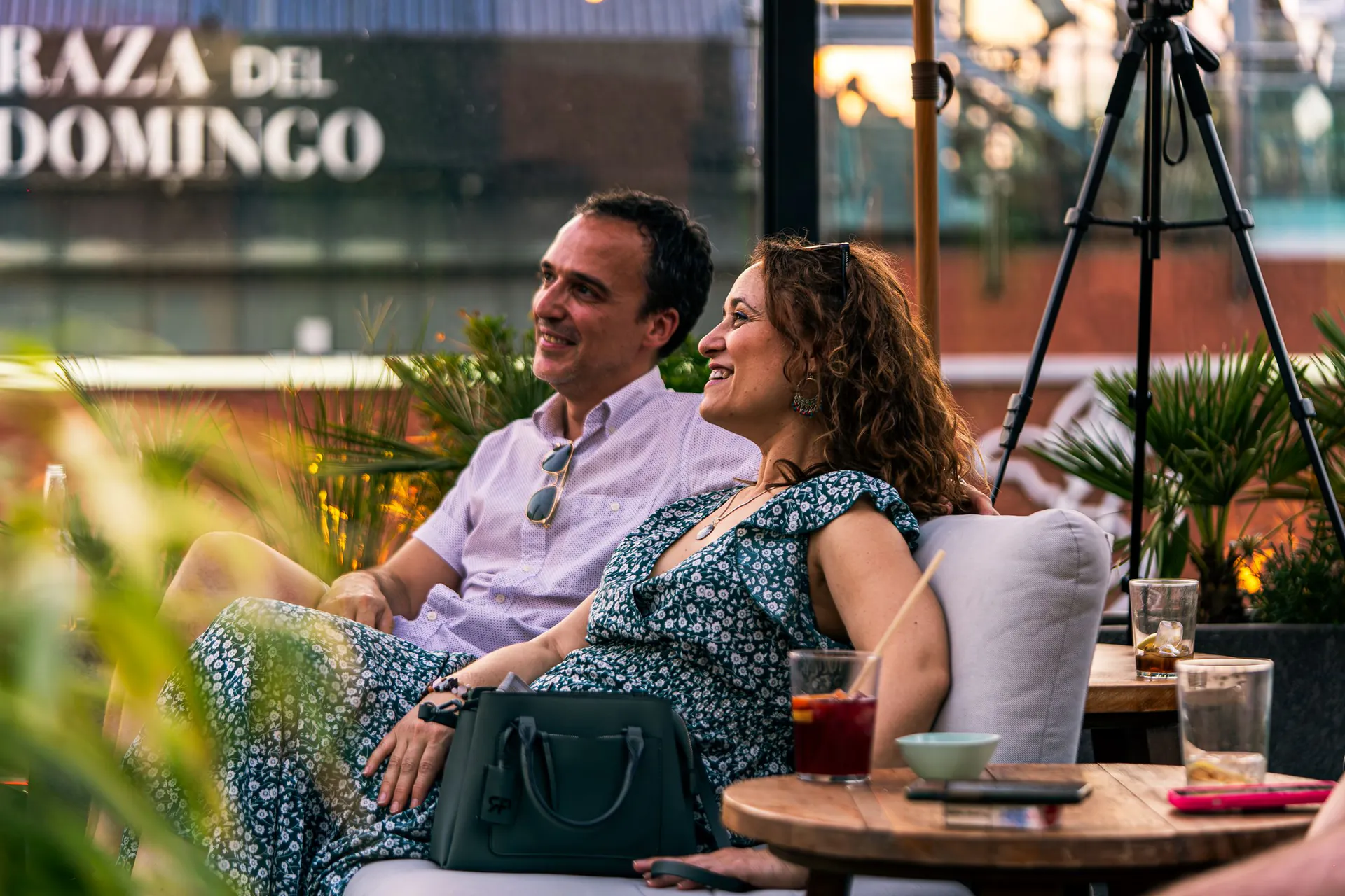Un homme et une femme d'une quarantaine d'années sourient, assis côte à côte sur une terrasse au coucher du soleil