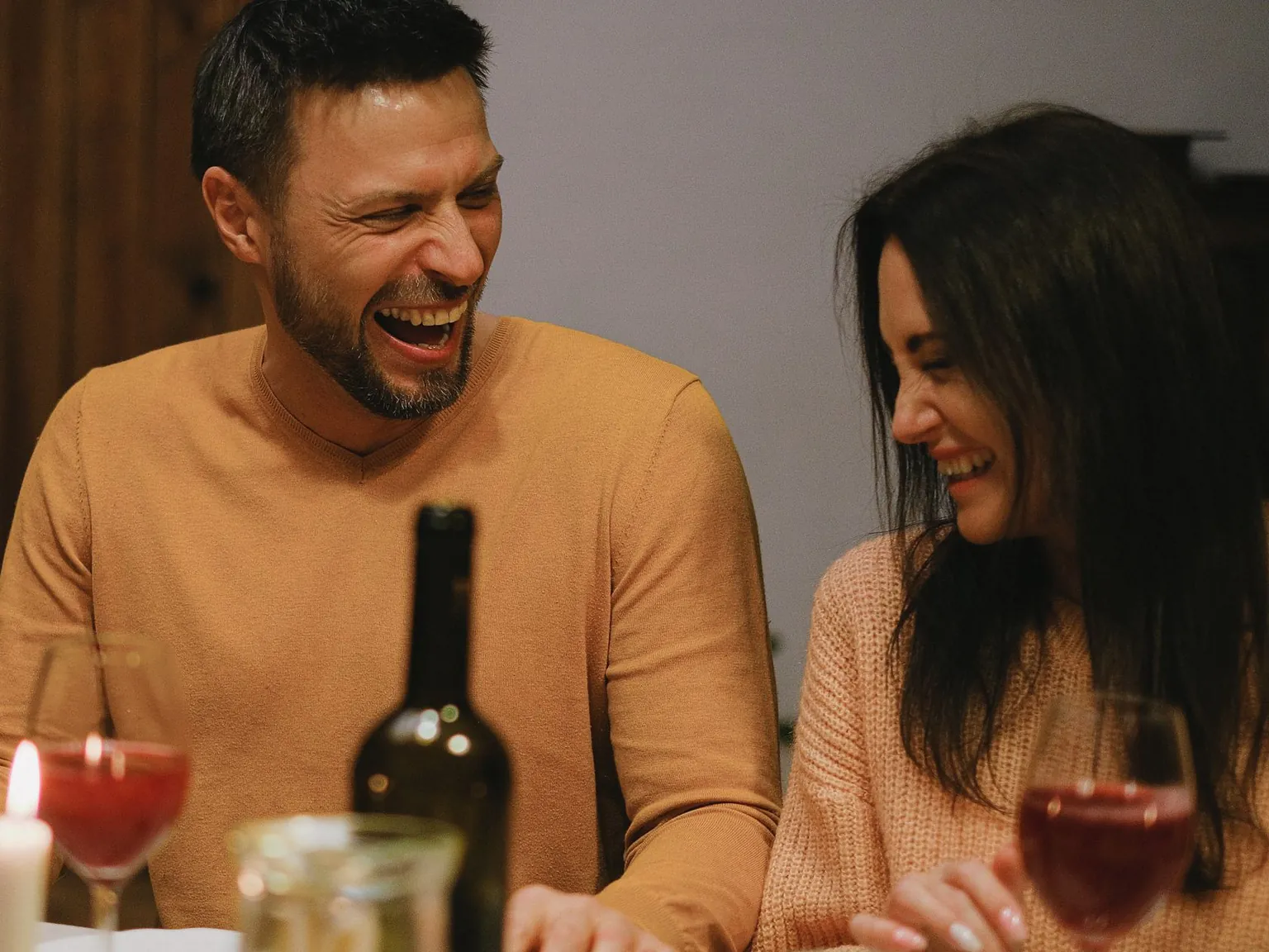 Un homme et une femme d'une quarantaine d'années rient ensemble lors d'un dîner aux chandelles, un verre de vin à la main