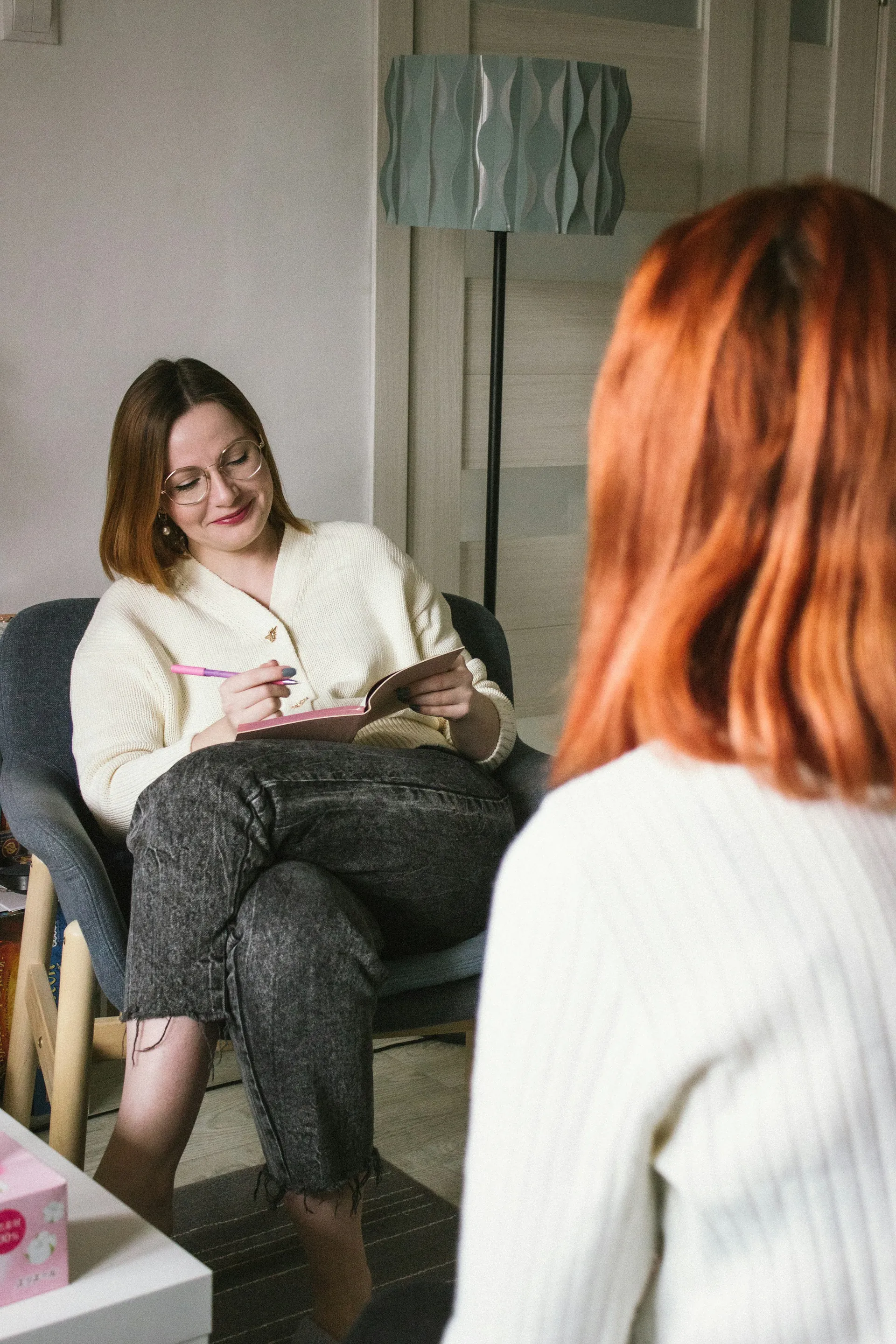 Une ambassadrice souriante, carnet et stylo en main, écoute une femme assise en face d'elle dans un salon