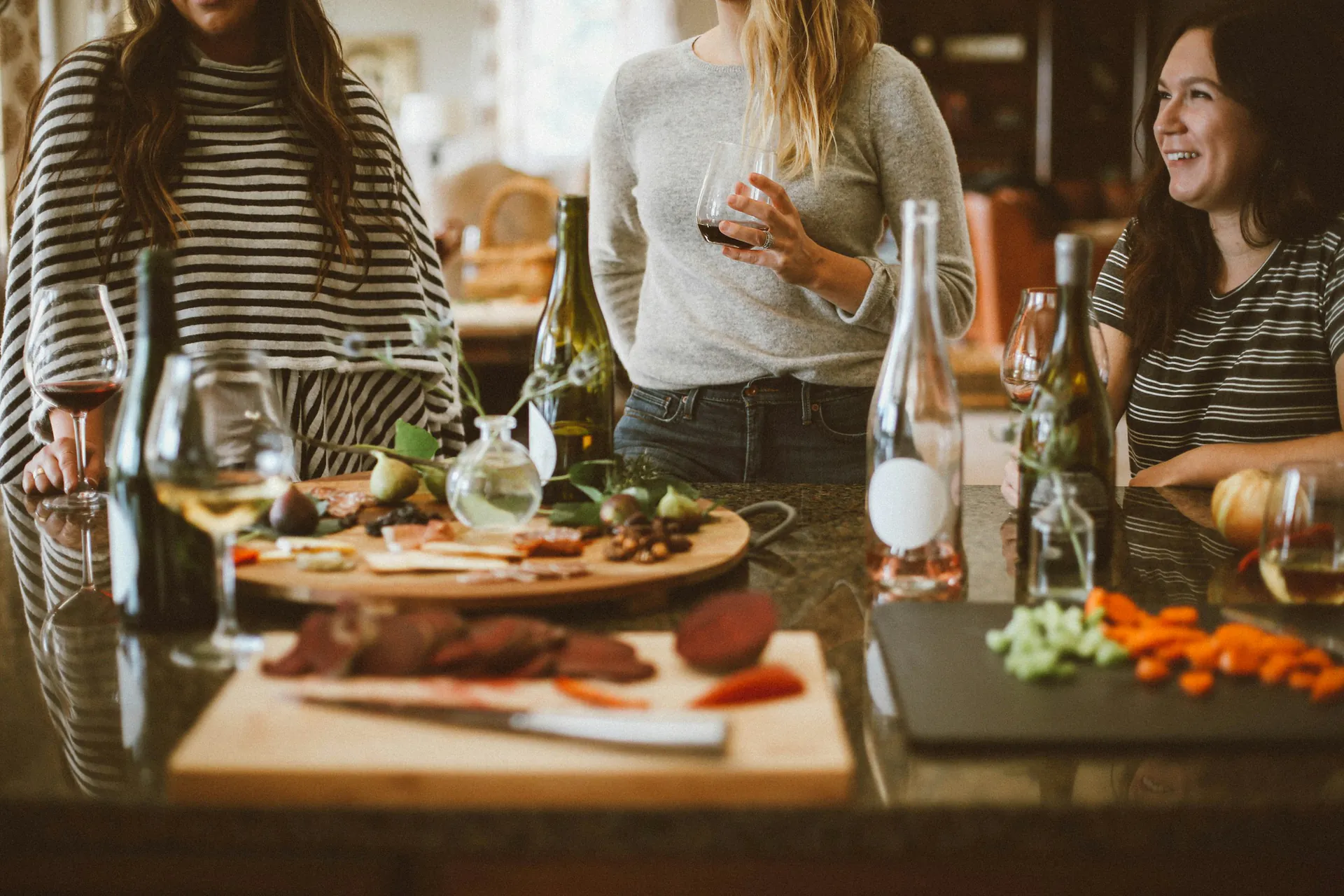 Trois amies préparent une table conviviale, un verre à la main